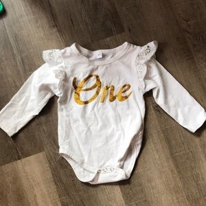 Baby girl onesie shirt with gold lettering spells “one” frill detail on sleeve